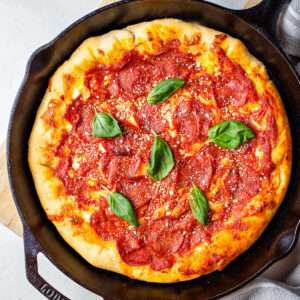 Pizza baked in a cast iron skillet with pepperoni and fresh basil leaves on top.