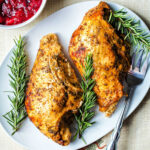Oven roasted turkey breast removed from the bone and placed on a platter with rosemary sprigs and cranberry sauce on the table.