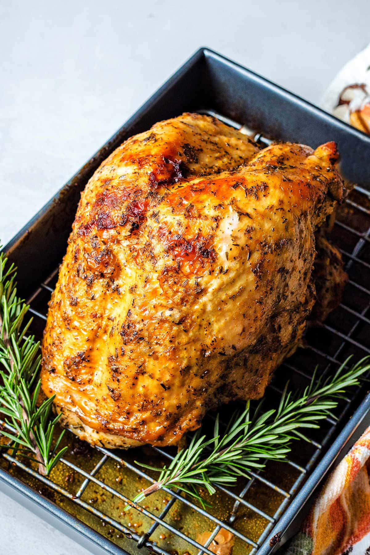 Oven roasted turkey breast in a baking dish with rosemary sprigs.