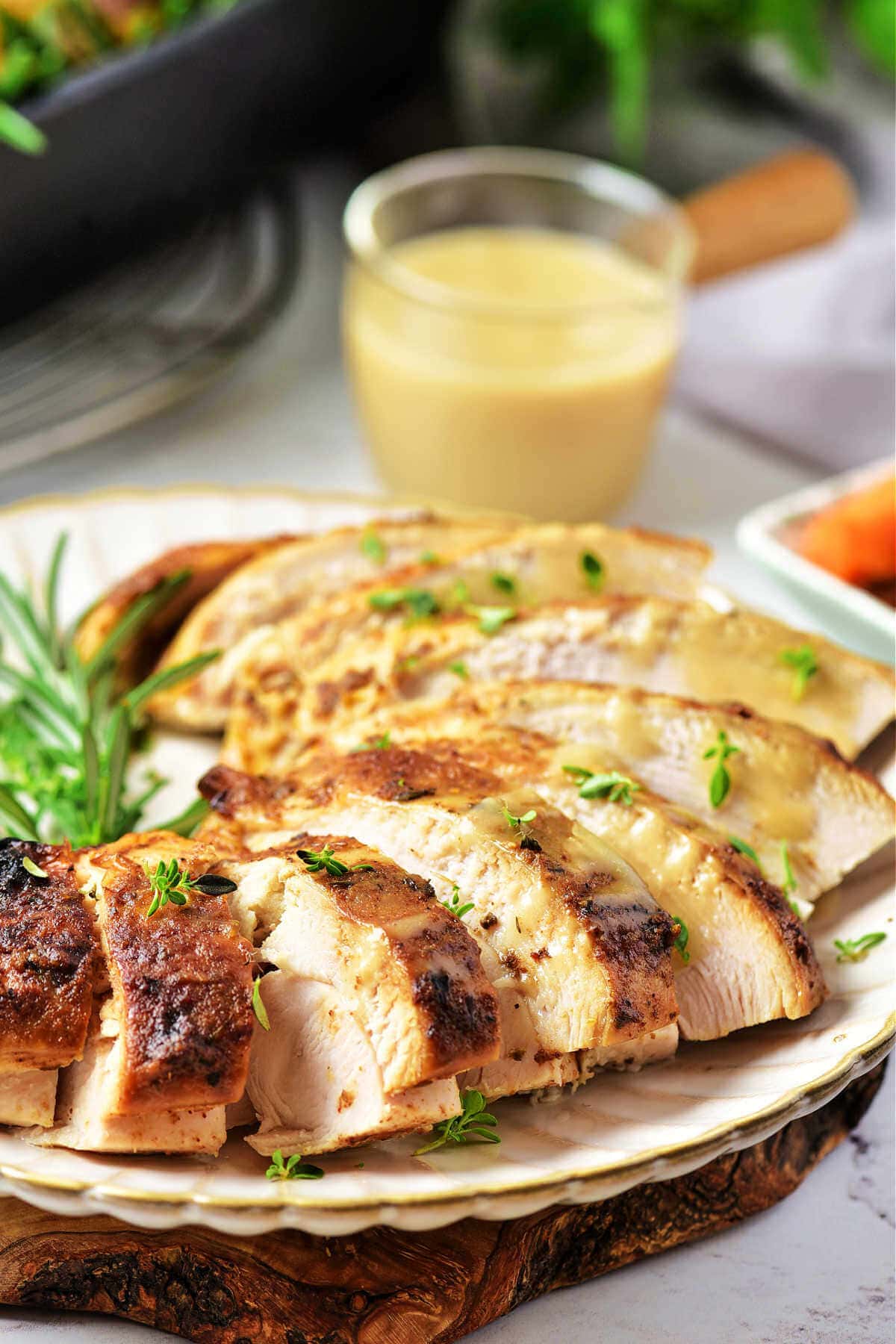 Slices of oven roasted turkey breast on a plate garnished with fresh herbs on a table with a bowl of gravy.