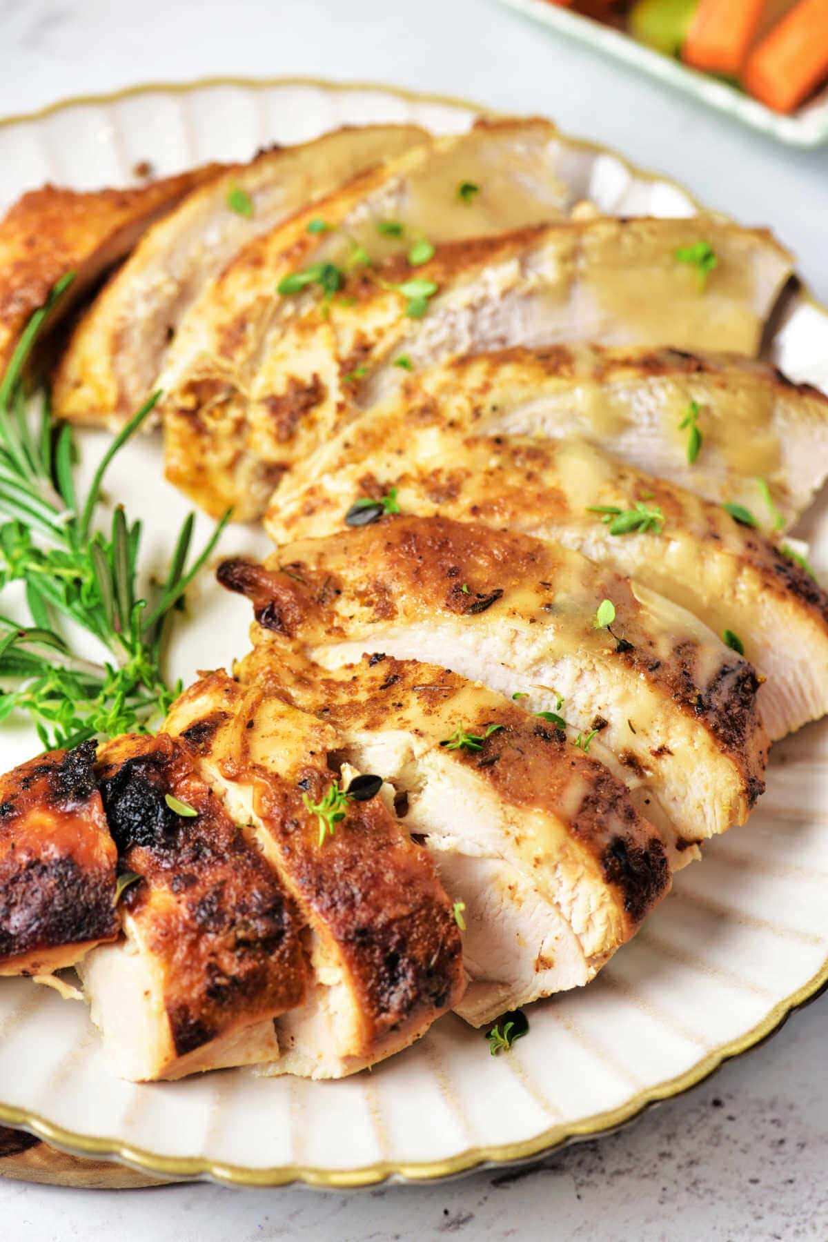 Slices of oven roasted turkey breast on a plate garnished with fresh rosemary.