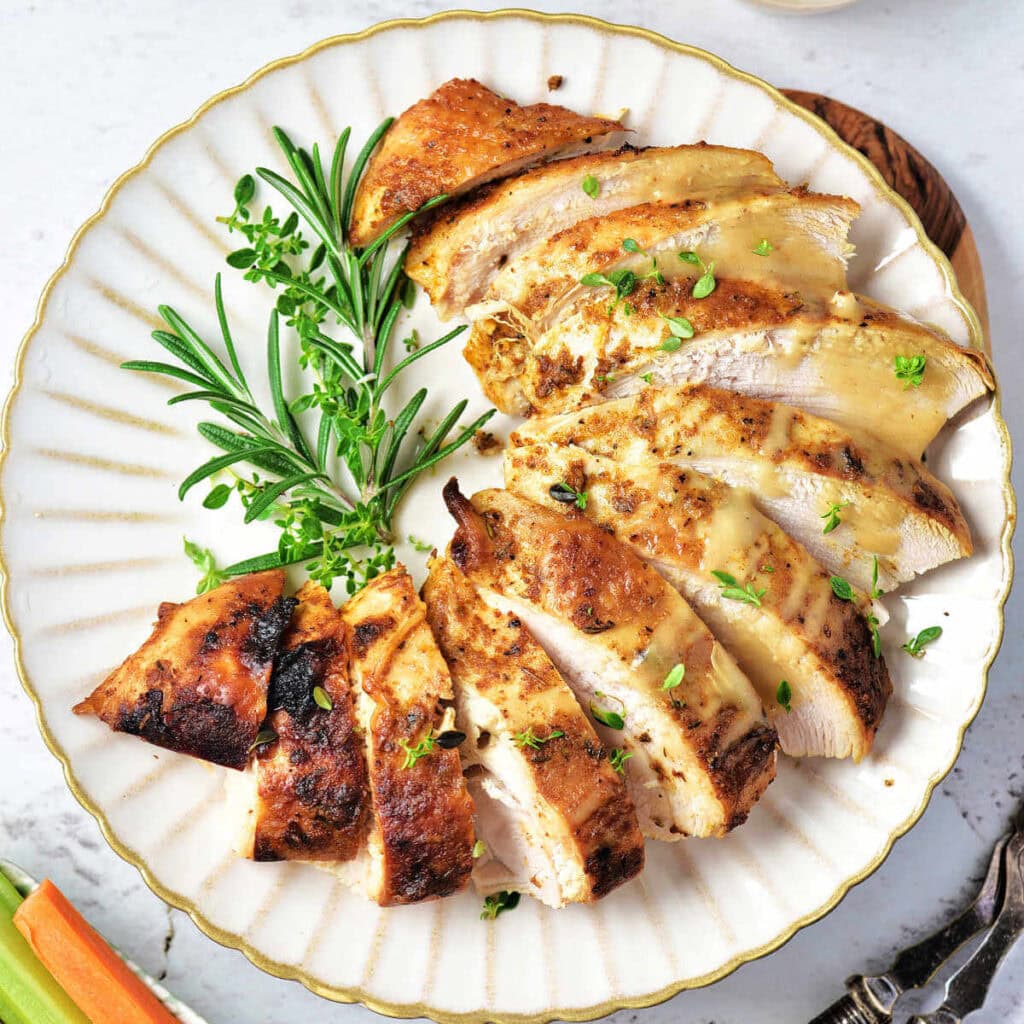 Slices of oven roasted turkey breast on a plate garnished with fresh herbs.