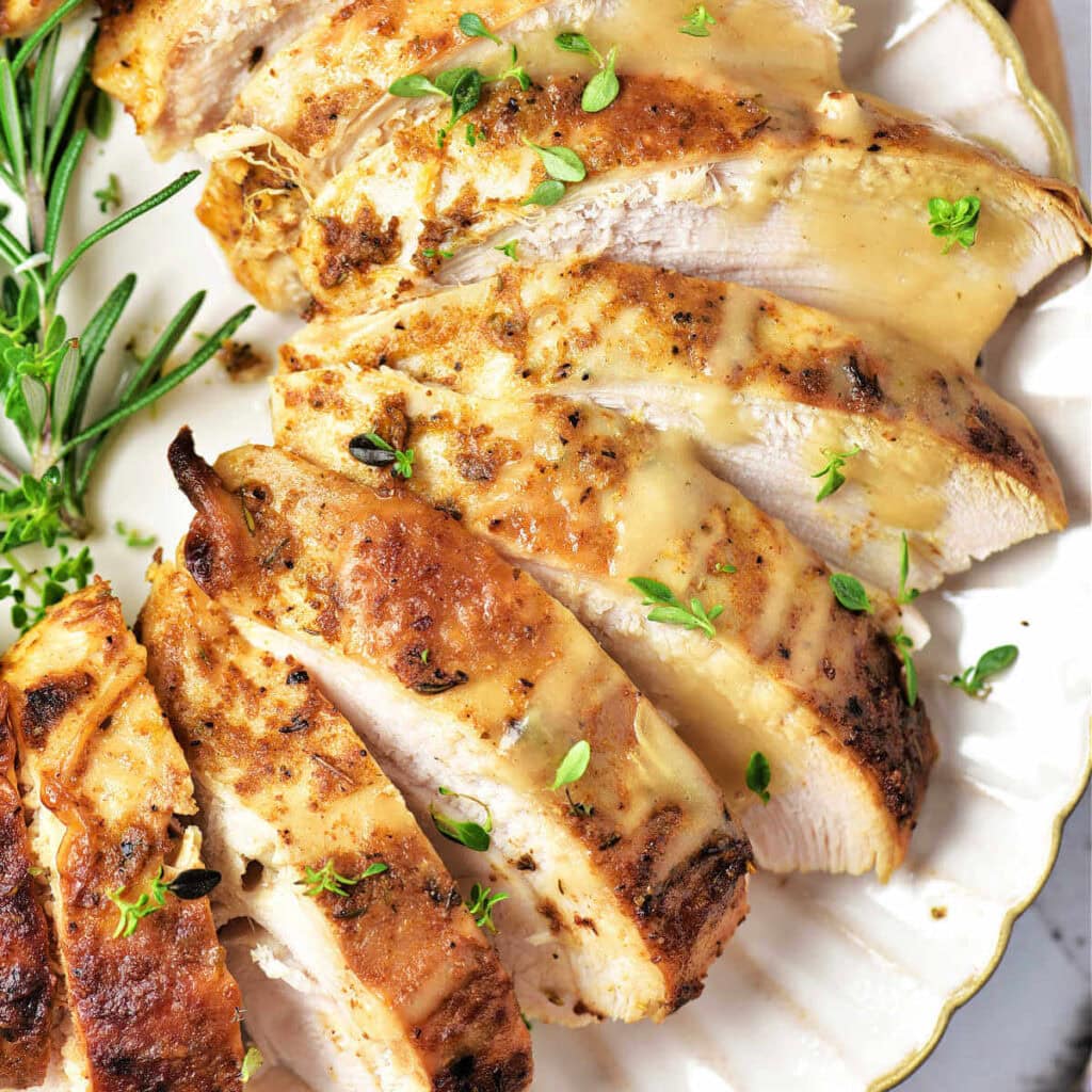 Slices of oven roasted turkey breast on a plate garnished with fresh herbs.