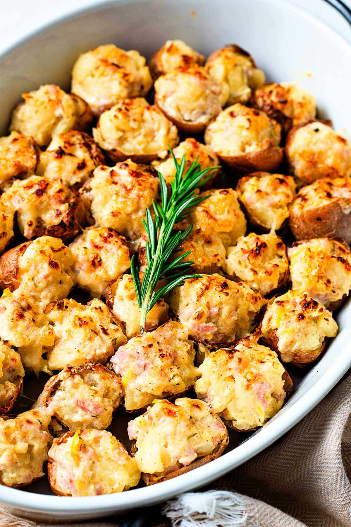 A baking dish of stuffed potato bites with a sprig of rosemary laying on top.