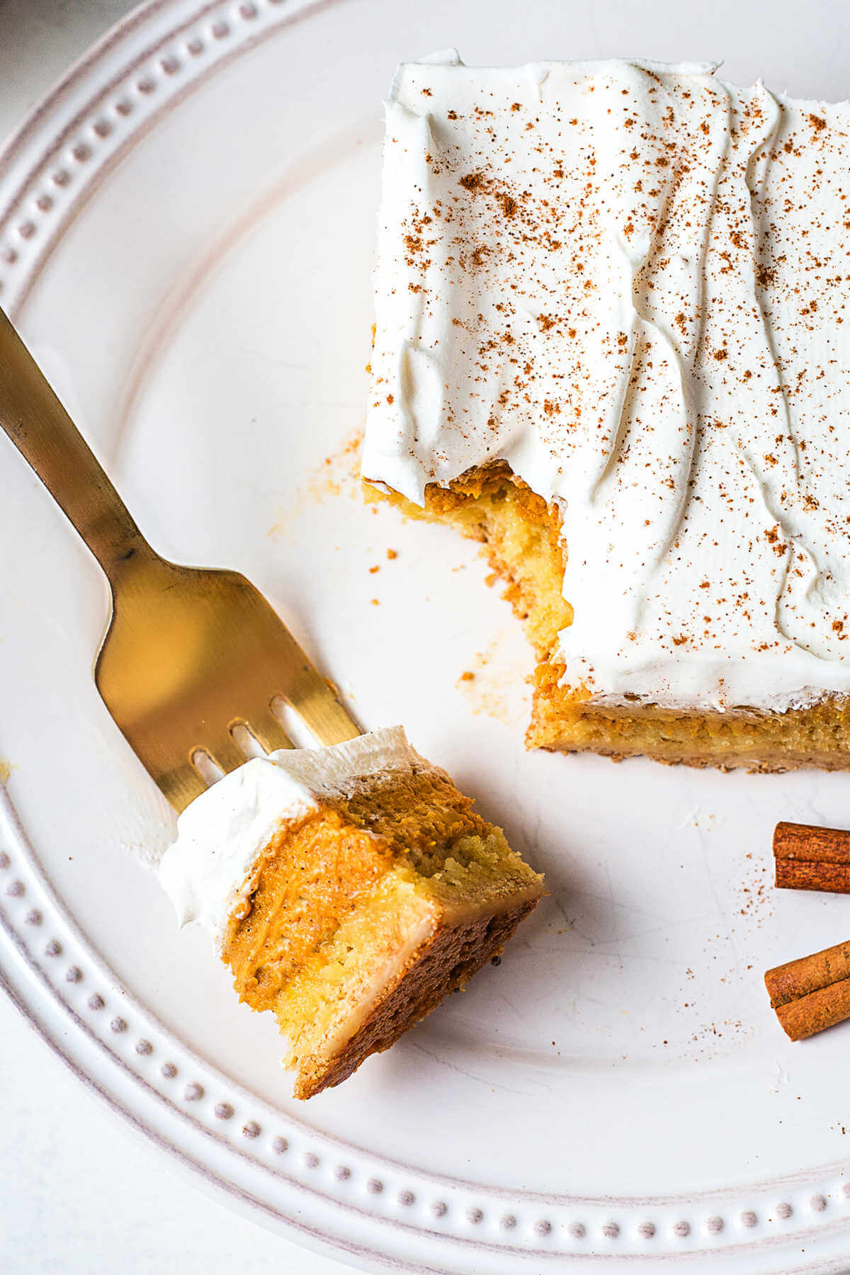 A bite of pumpkin dessert on a fork resting on a plate.