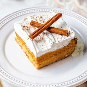 A slice of pumpkin dessert on a plate garnished with cinnamon sticks on a table.