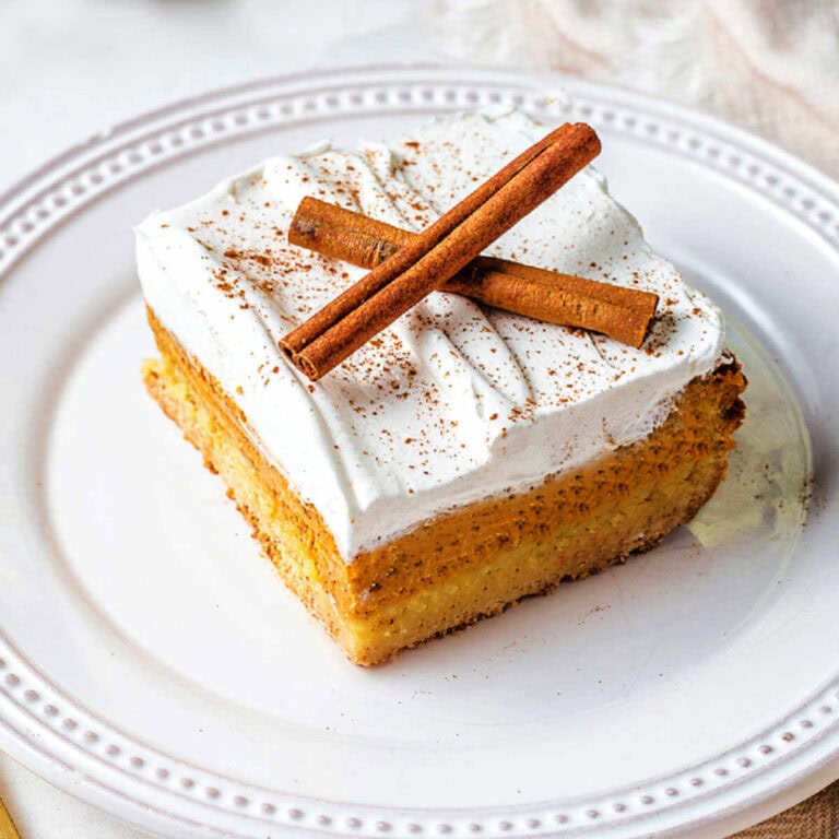 A slice of pumpkin dessert on a plate garnished with cinnamon sticks on a table.