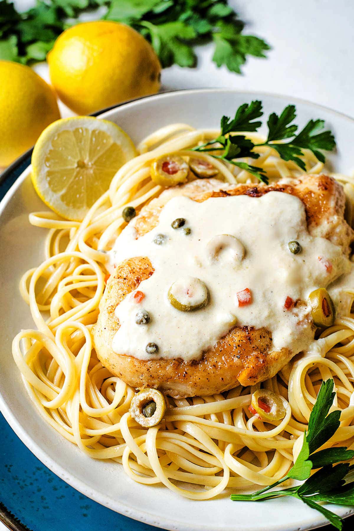 Lemon parmesan sauce with capers and olives ladled over a chicken cutler and linguine.