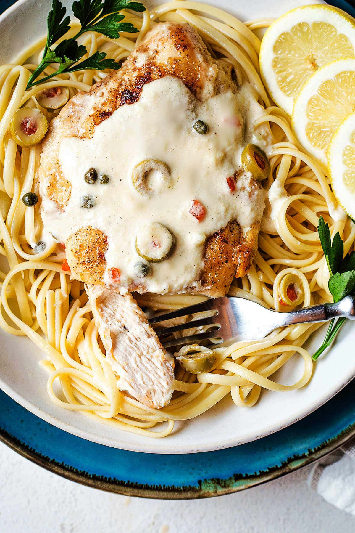 A slice of chicken on a fork on a plate with pasta and sauce.