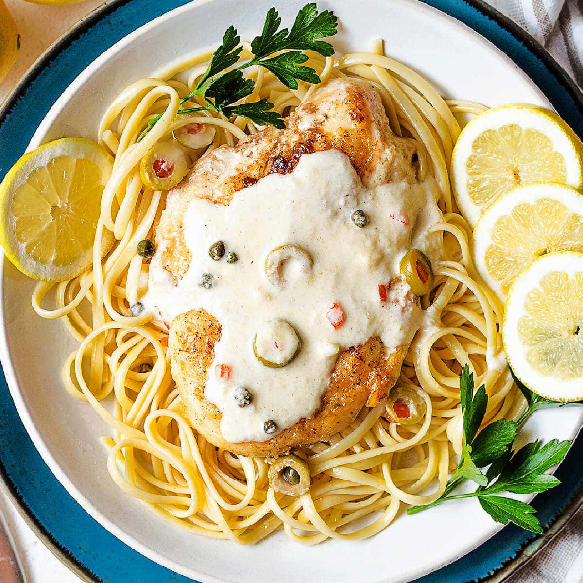 Scaloppine al limone over a bed of linguine with lemon slices and fresh parsley on the side of the plate.