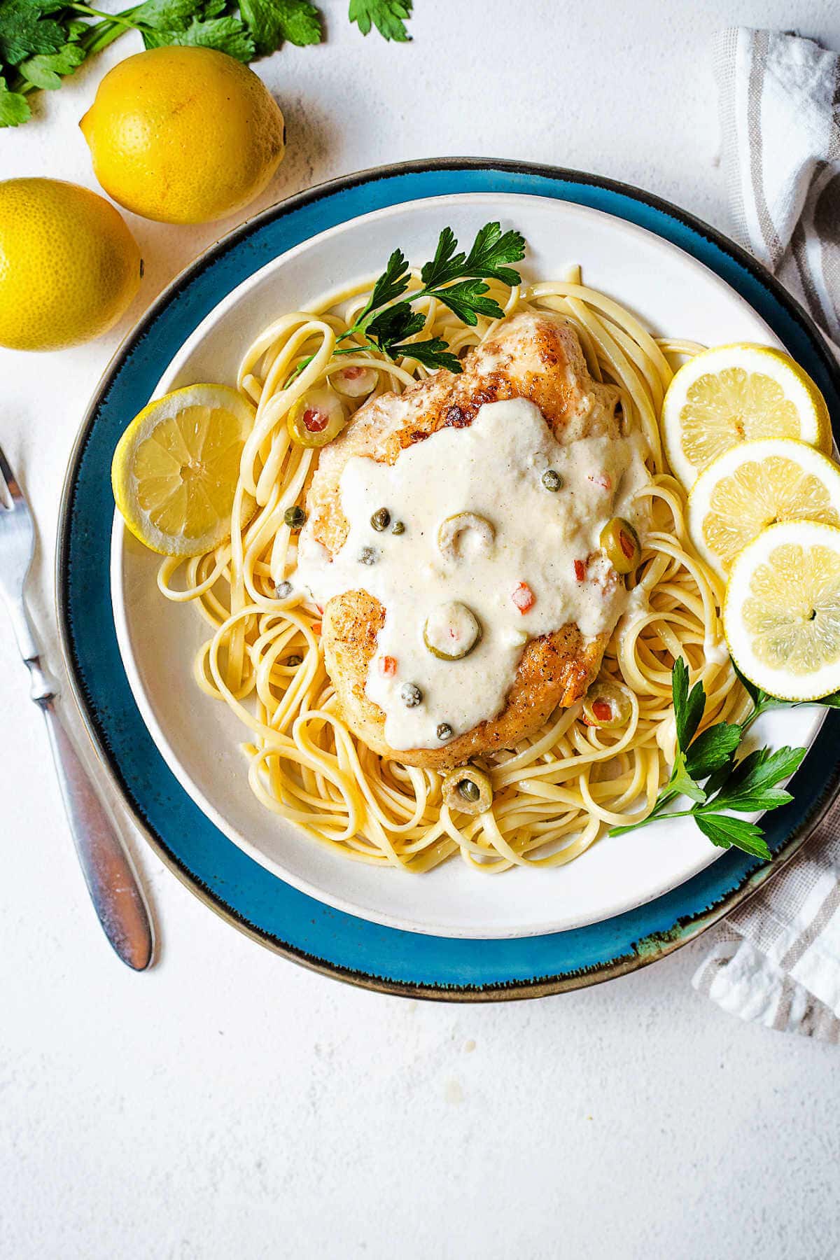 Scaloppine al limone over a bed of linguine on a plate with lemons on a table.