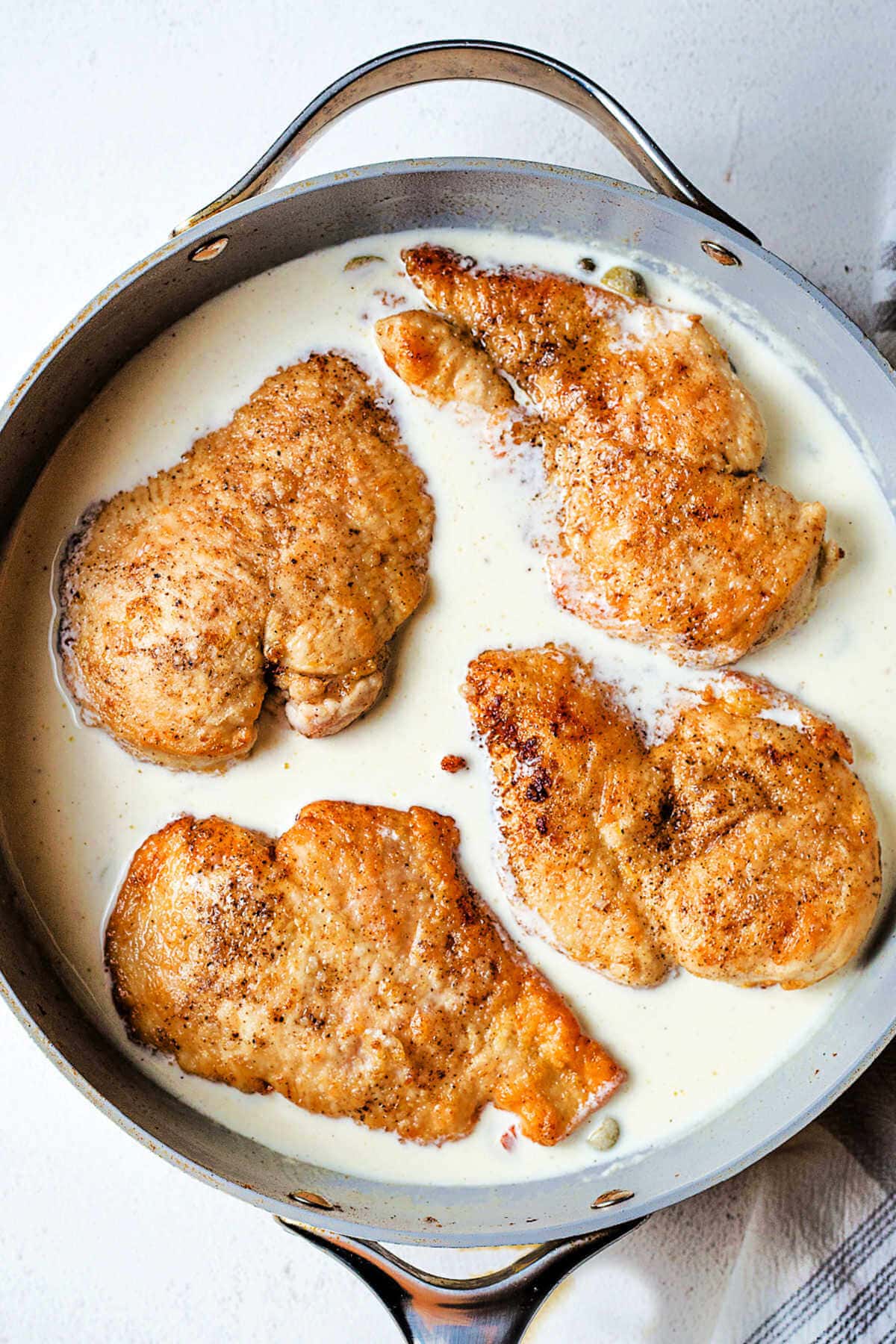 Cooked chicken cutlets nestled in lemon cream sauce in a large skillet.