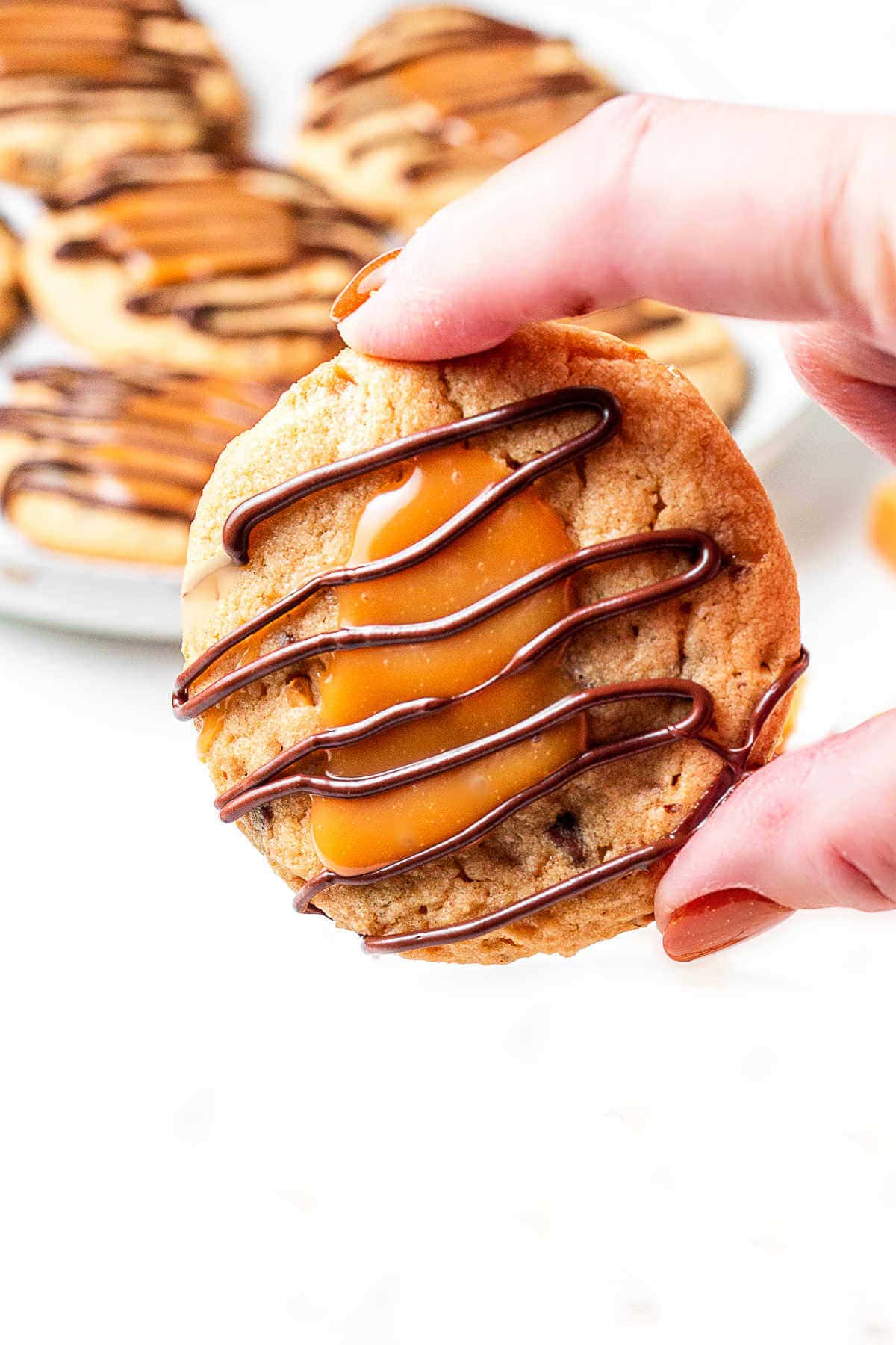 A close up shot of a hand holding a turtle cookie with more cookies in the background.