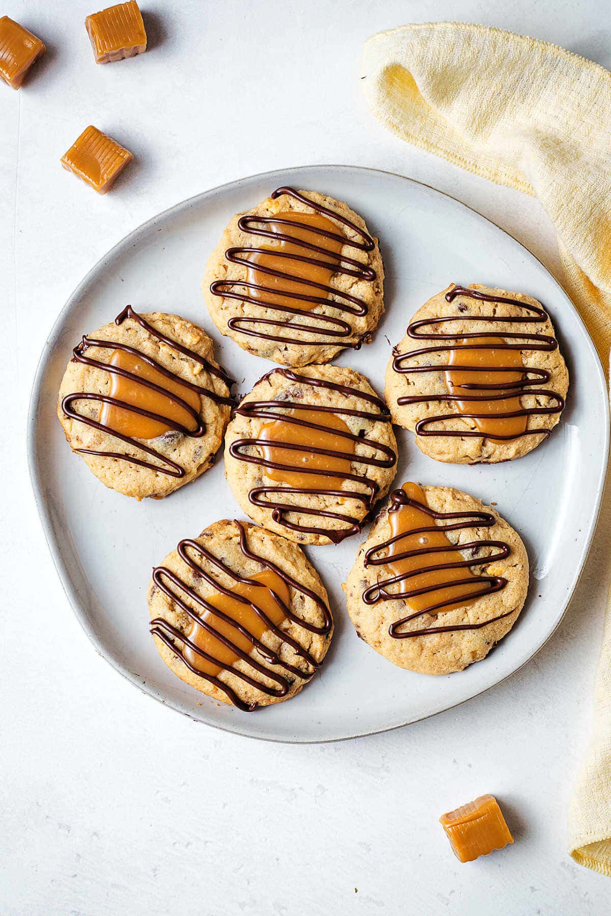 A plate of turtle cookies on a table with caramels scattered around.