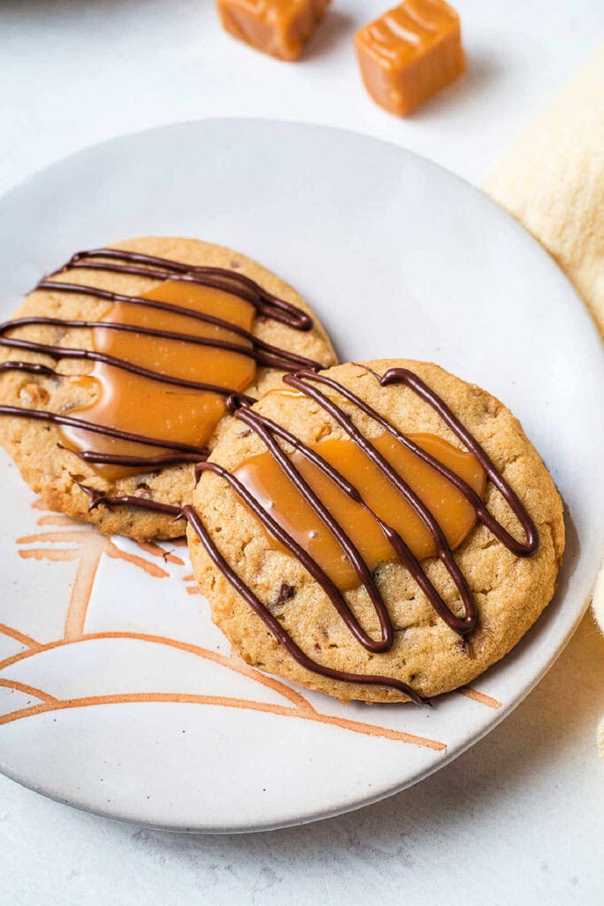 Two Toffee Turtle Cookies with chocolate drizzle on a serving plate.