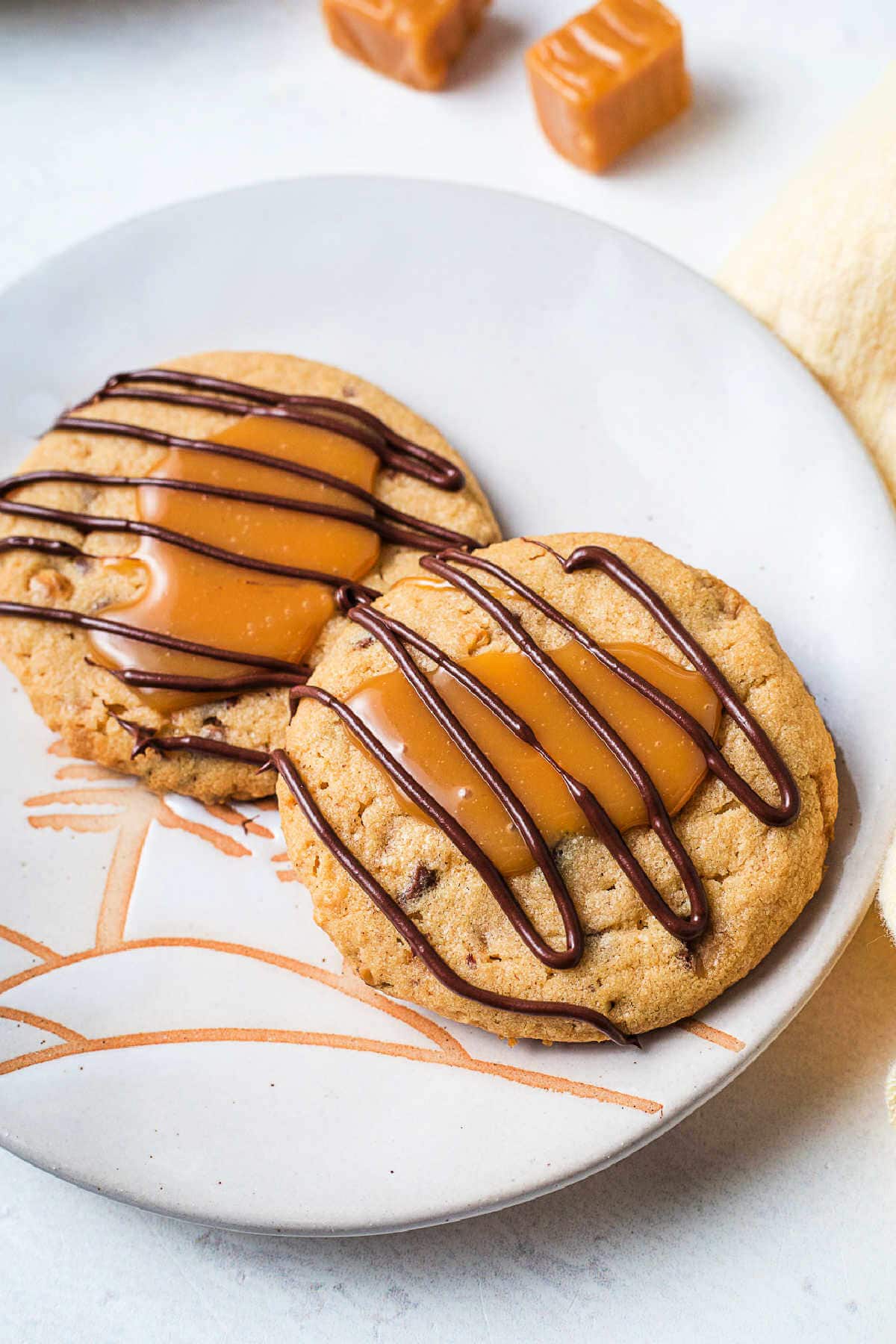 Two Toffee Turtle Cookies with chocolate drizzle on a serving plate.