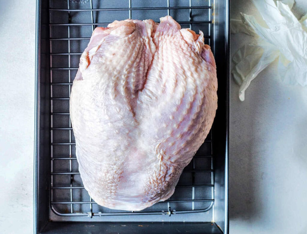Uncooked turkey breast. in a roasting pan with a rack.