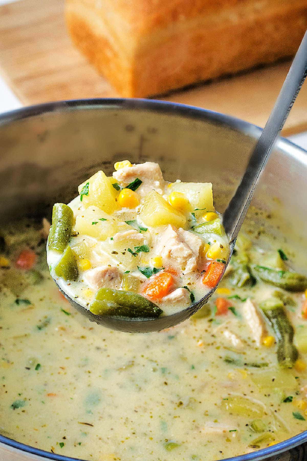 A ladle lifting out a scoop of chicken soup from a pot on a table.