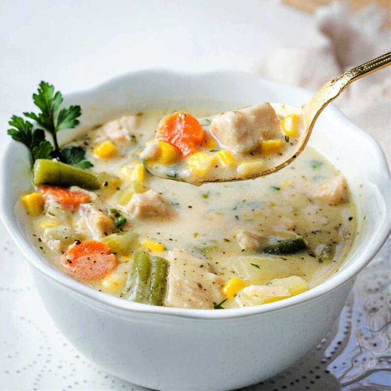 A spoon lifting up a bite of Chicken Vegetable soup out of a bowl on a table,