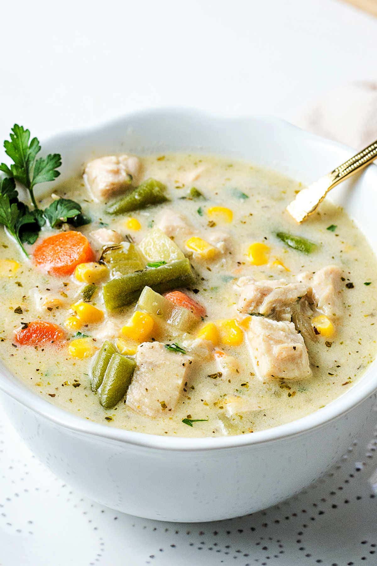 A bowl of creamy chicken vegetable soup on a table garnished with a sprig of fresh parsley.