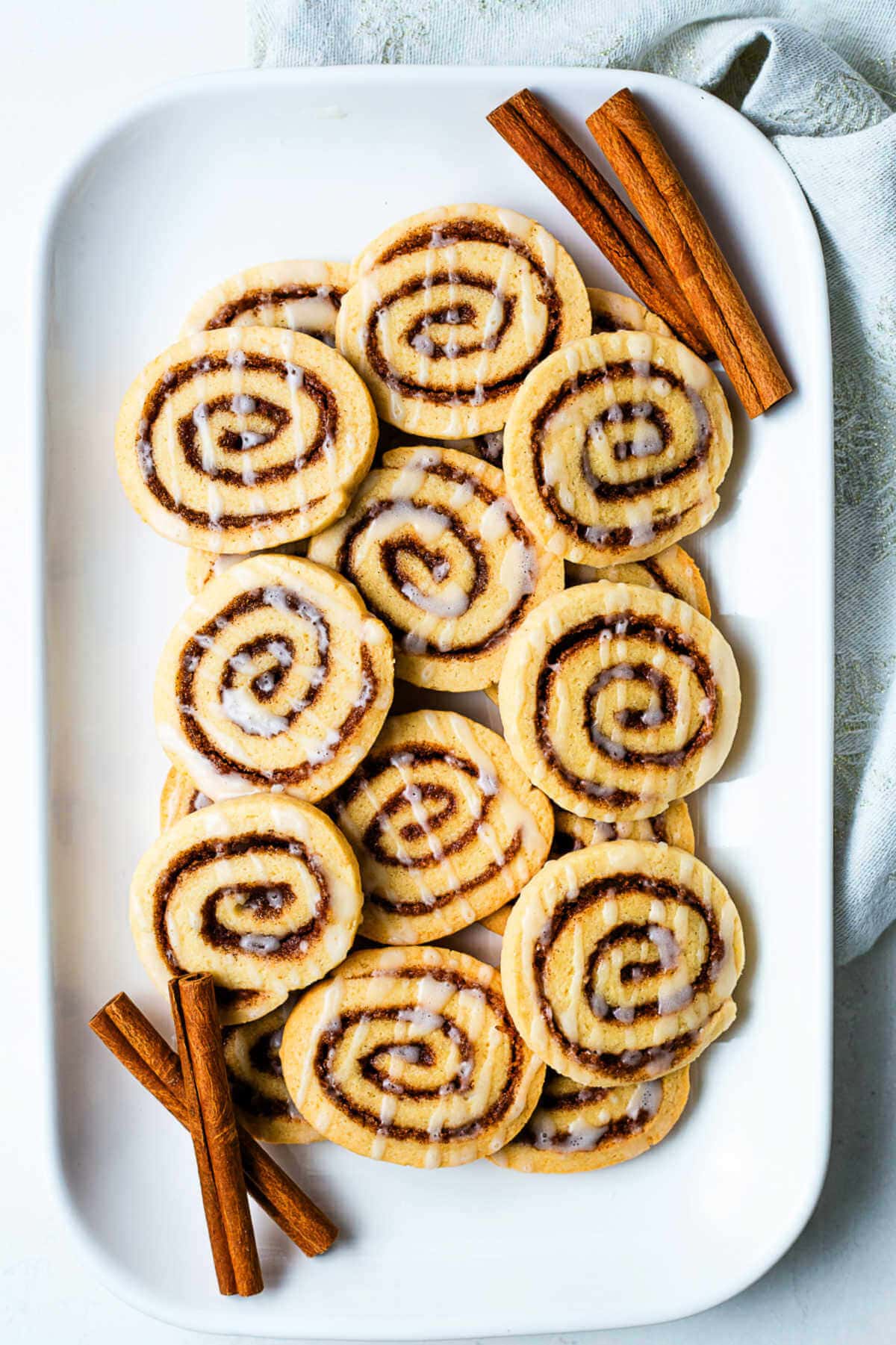 A platter of cinnamon roll cookies garnished with cinnamon sticks on a table.