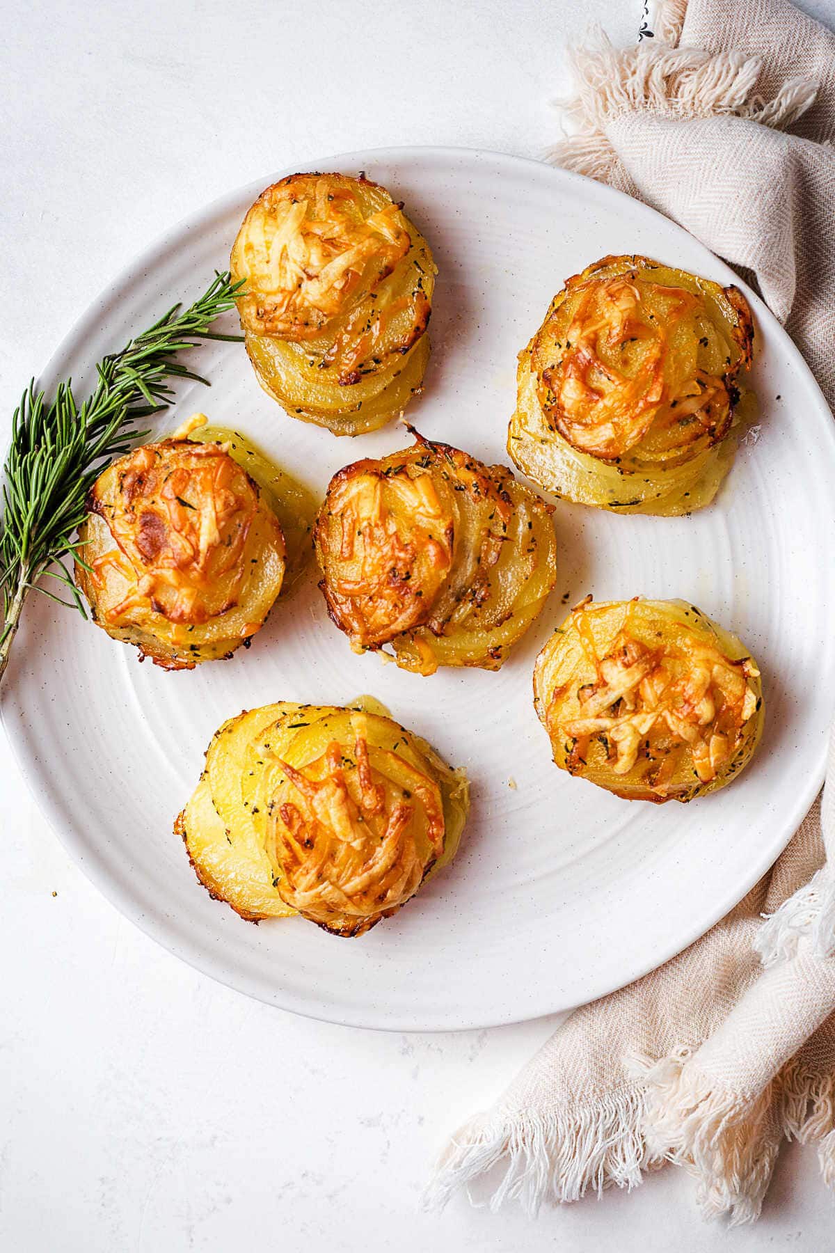 Potaqto Stacks on a serving plate with a sprig of rosemary on a table.