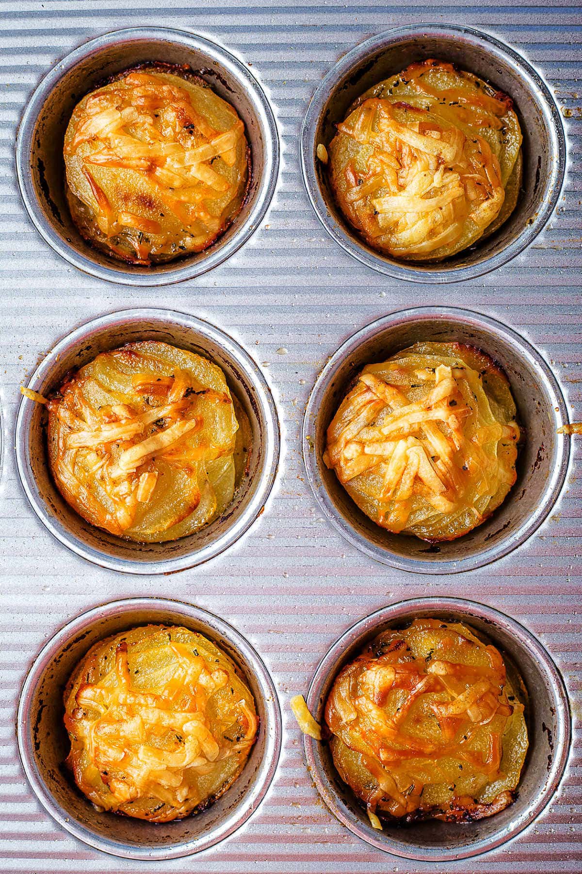 Potato Stacks in a muffin tin with golden brown cheese on top.