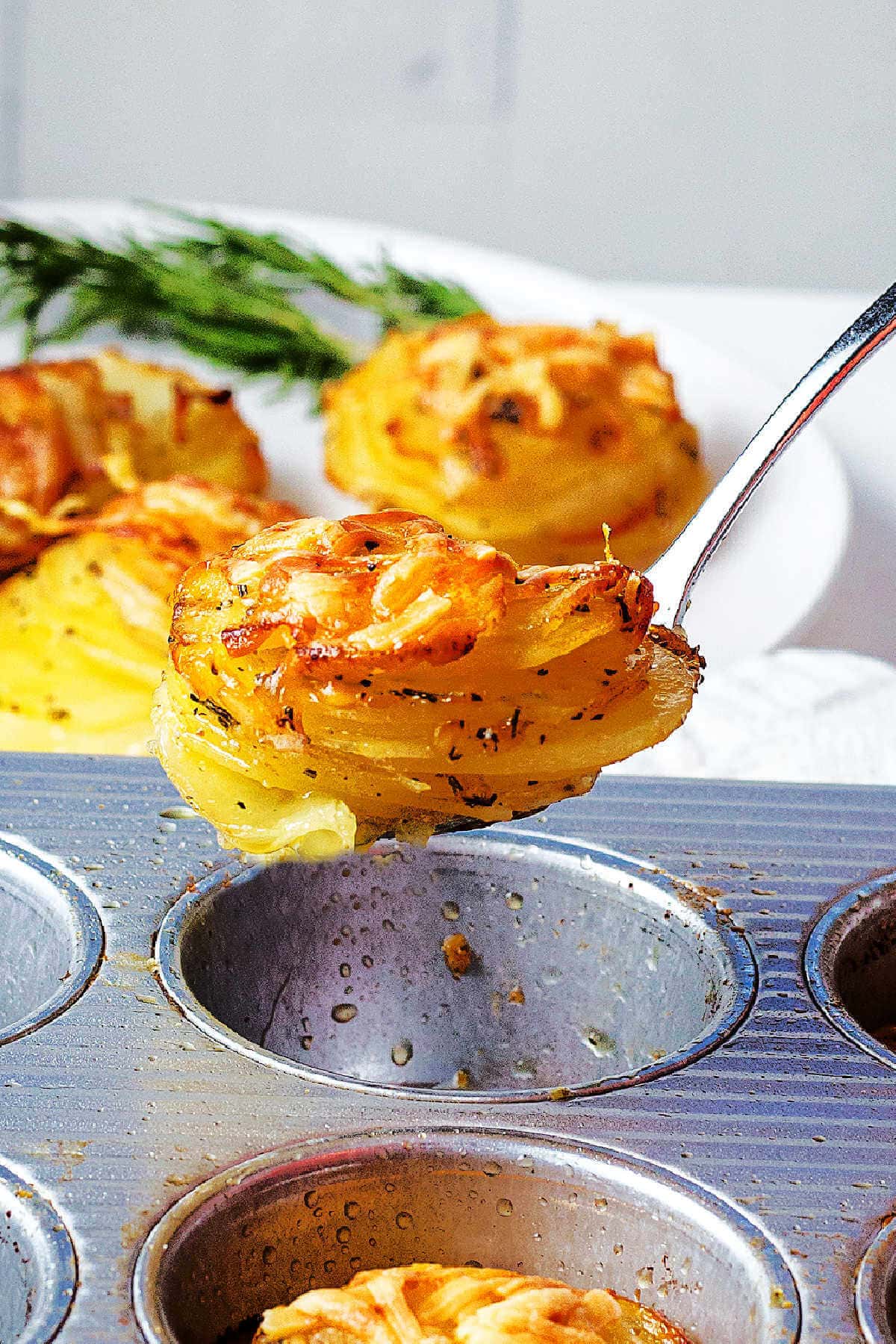 Lifting potato stacks out of a muffin tin with a soup spoon.