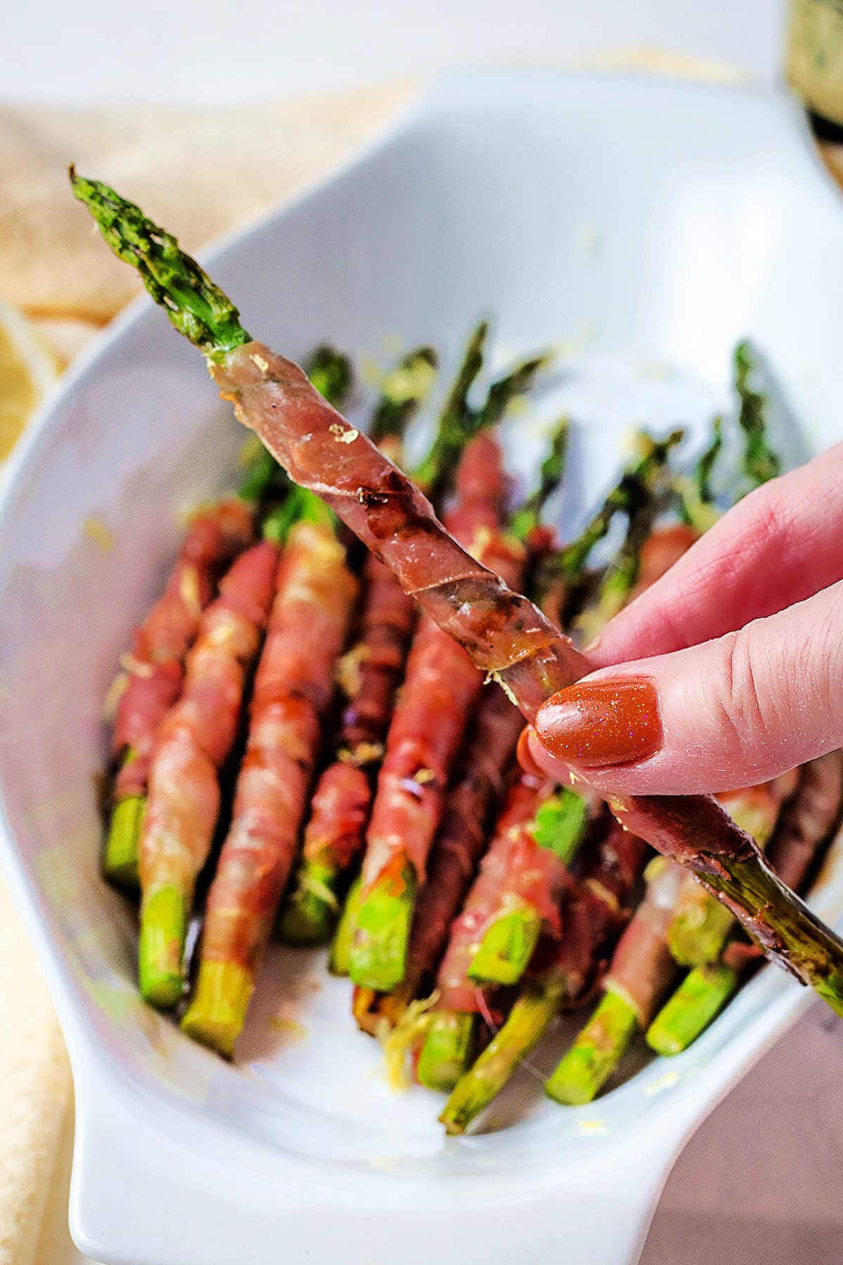 A hand holding a piece of prosciutto wrapped asparagus.