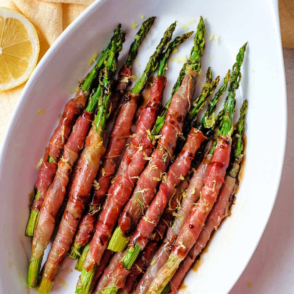 Crispy Prosciutto-Wrapped Roasted Asparagus Appetizer garnished with lemon zest on a serving platter on a table.