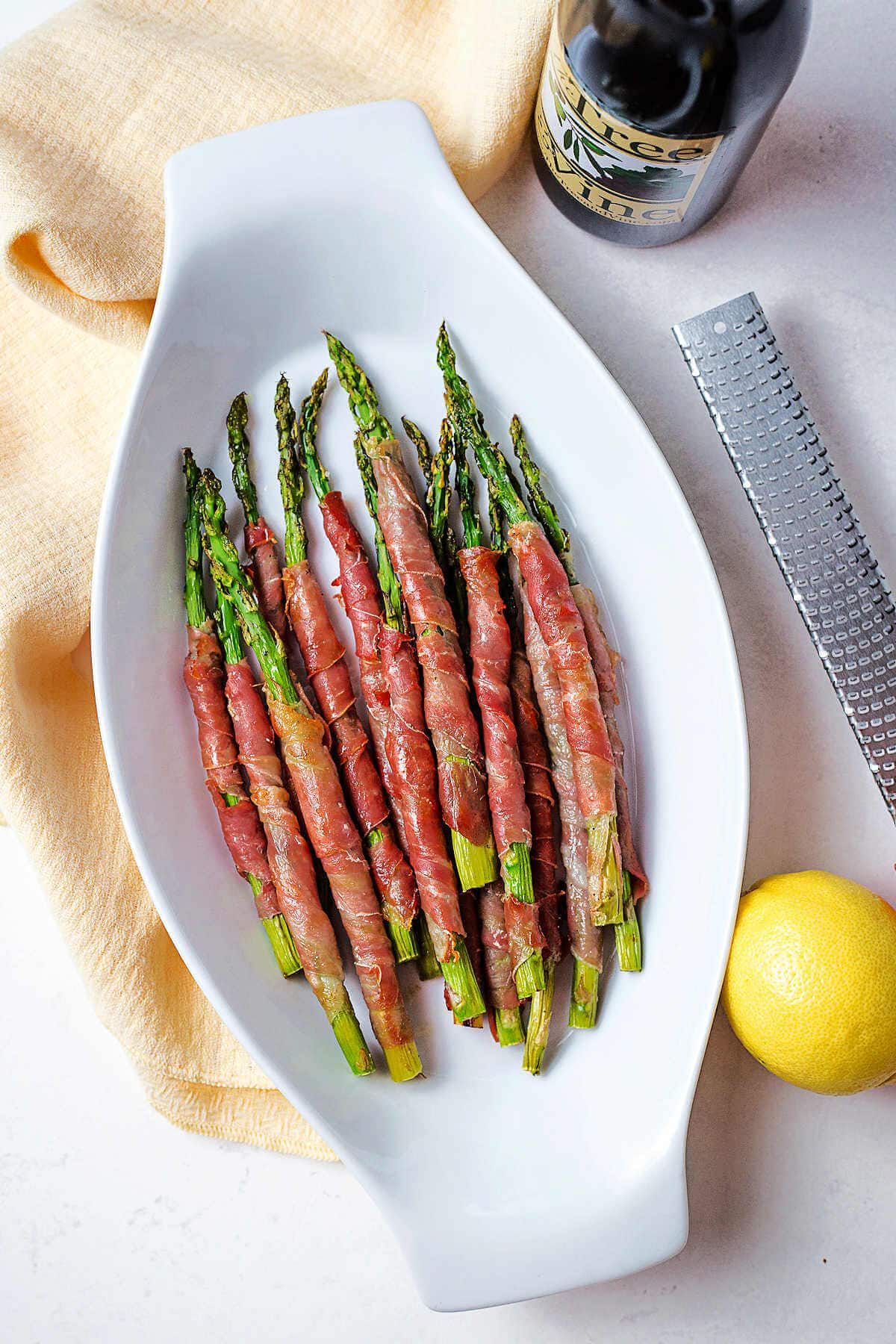 Asparagus in a serving dish with a lemon and zester to teh side on a table.