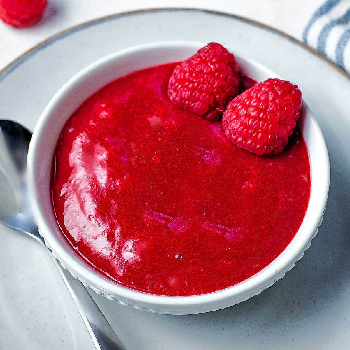 A bowl of raspberry coulis, dessert sauce, on a saucer on a table.