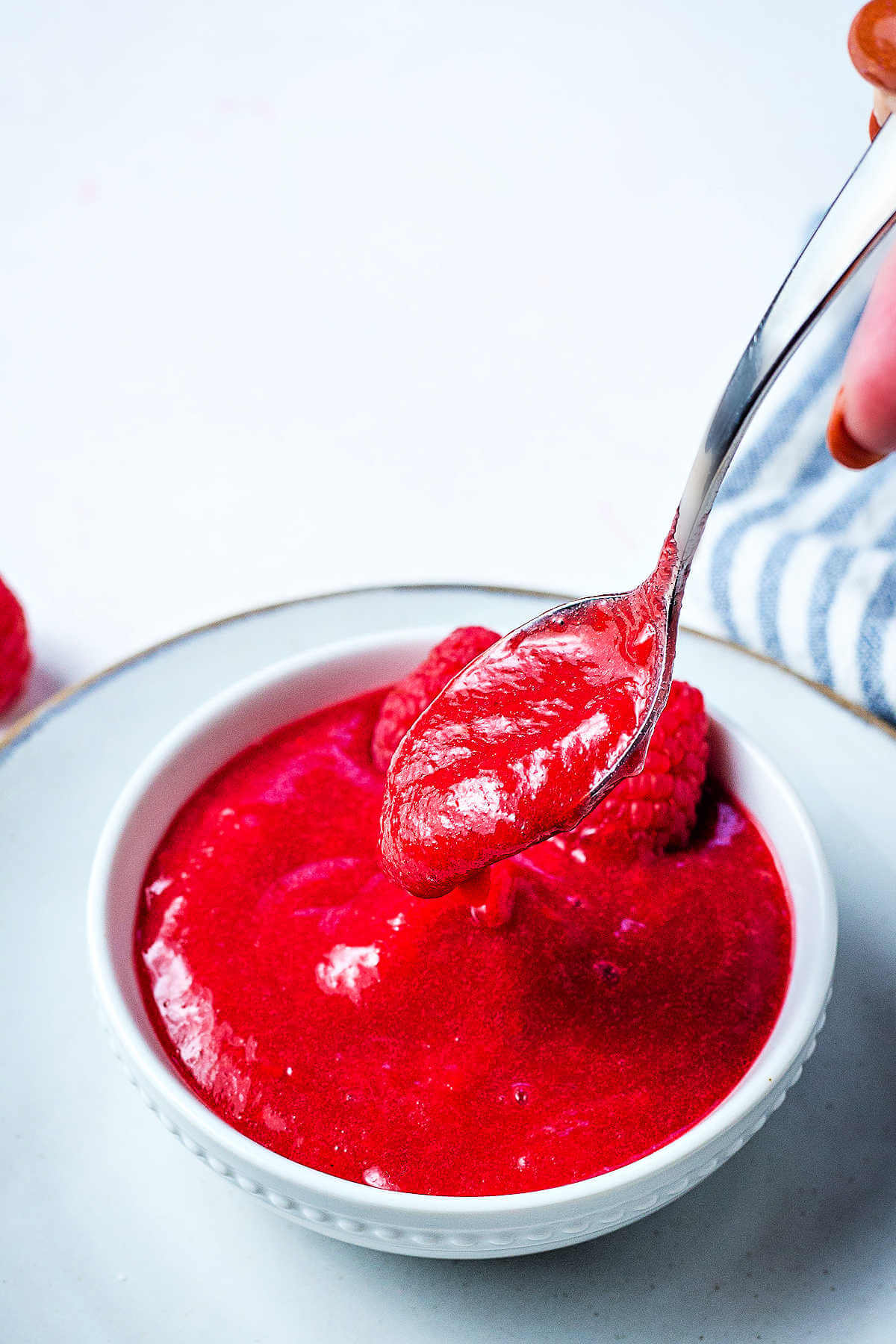 A spoon dipping raspberry sauce out of a bowl on a saucer.