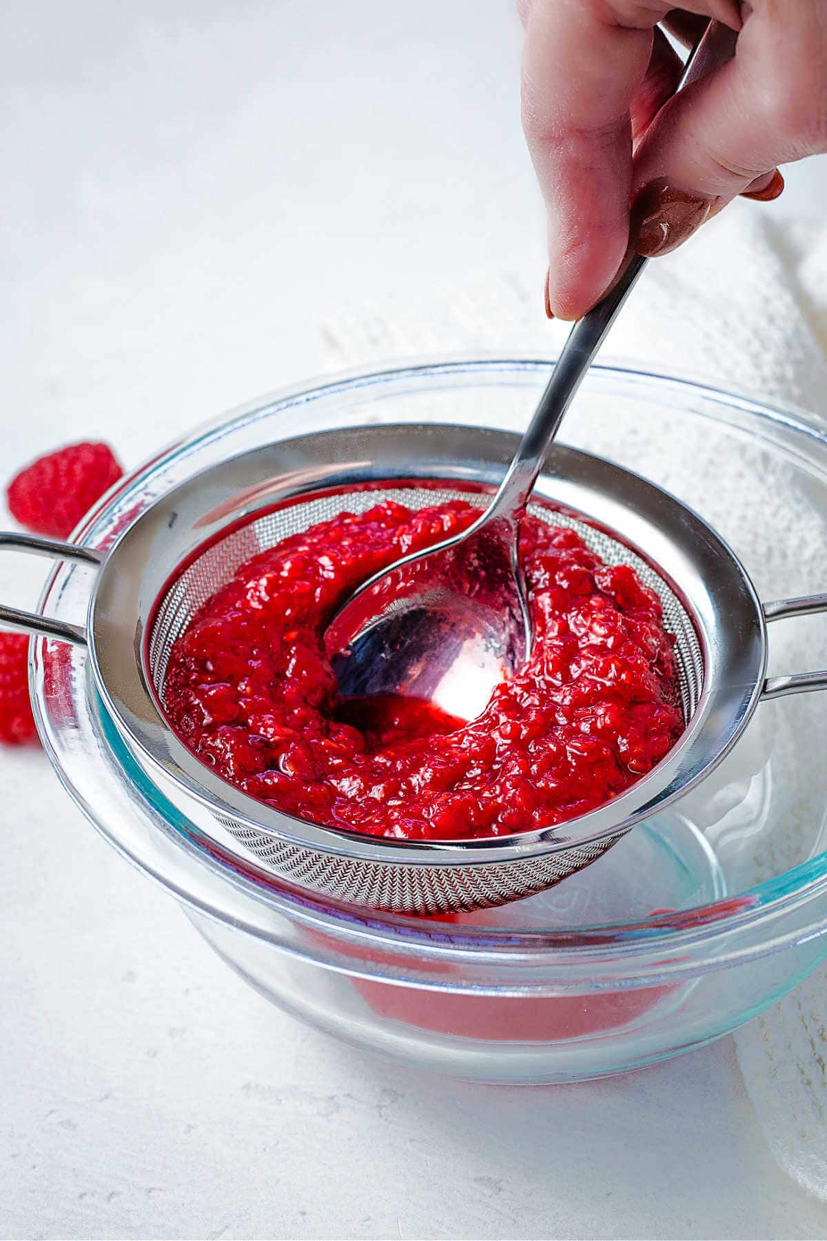 Pressing raspberry coulis through a fine mesh strainer with the back of a spoon to remove the seeds.