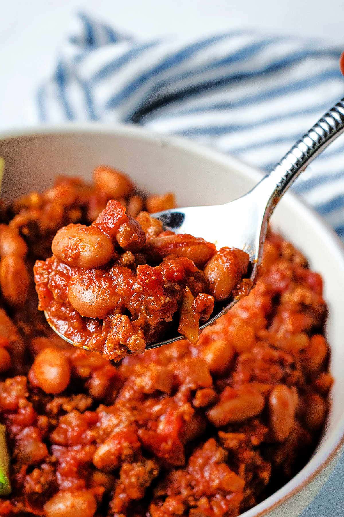 A spoon lifting a bite of red chili out of a bowl on a table.