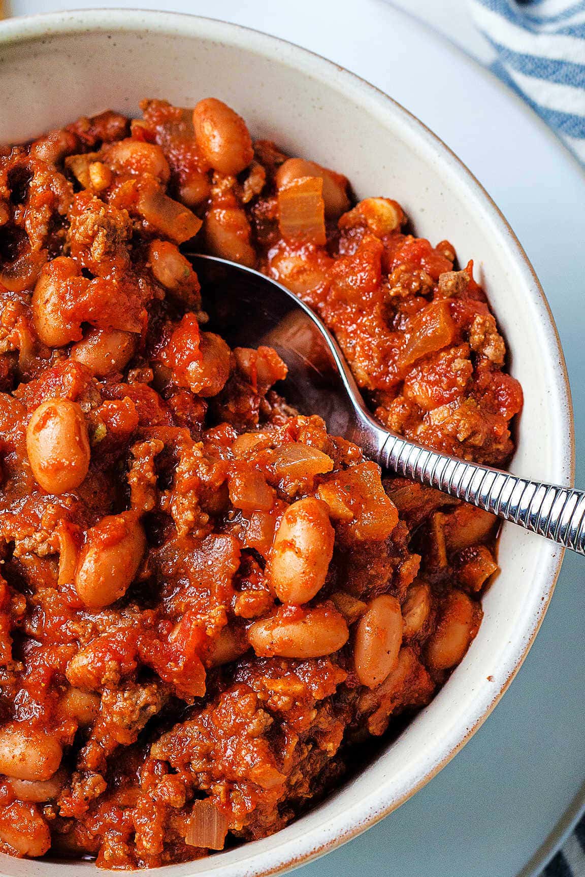 A bowl of red chili and a spoon on a table.