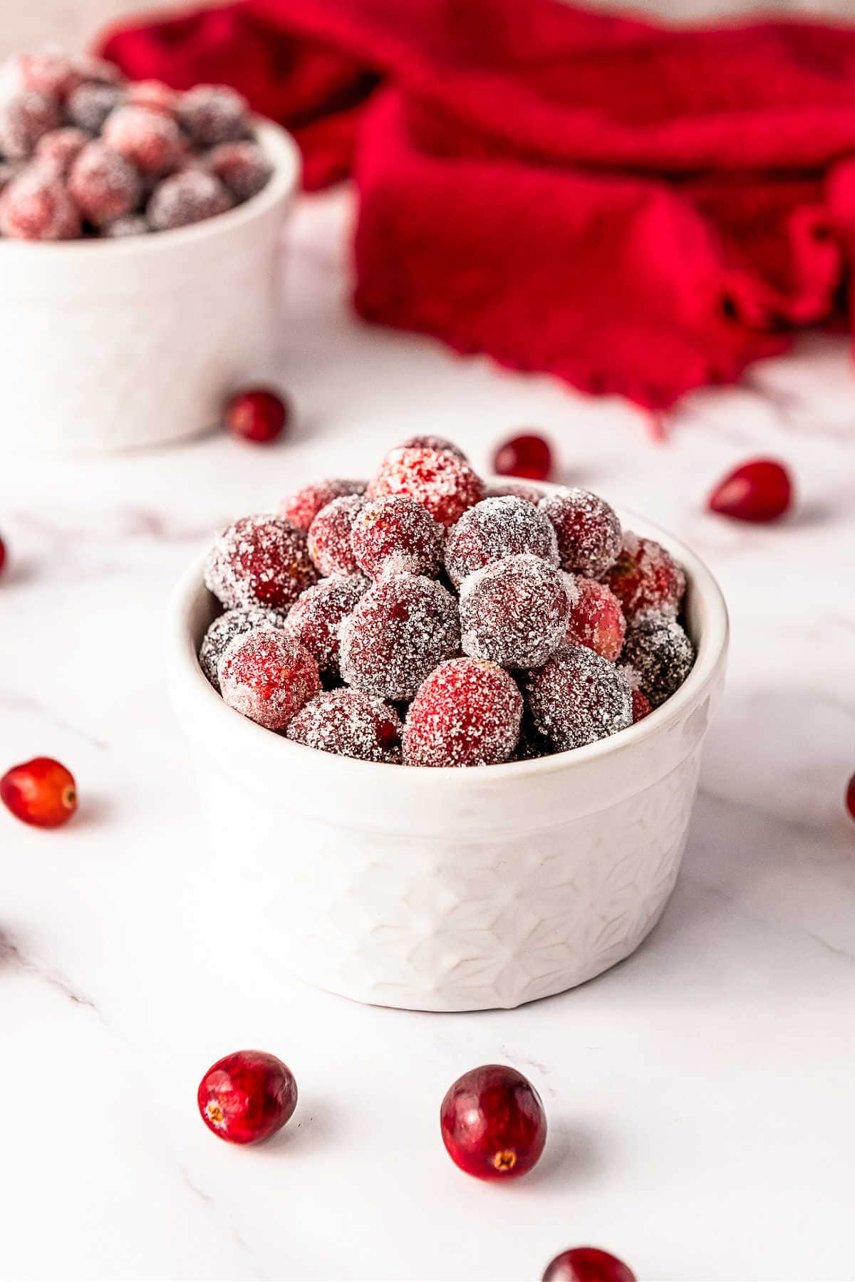 Bowls of candied cranberries on a table with cranberries scattered around.