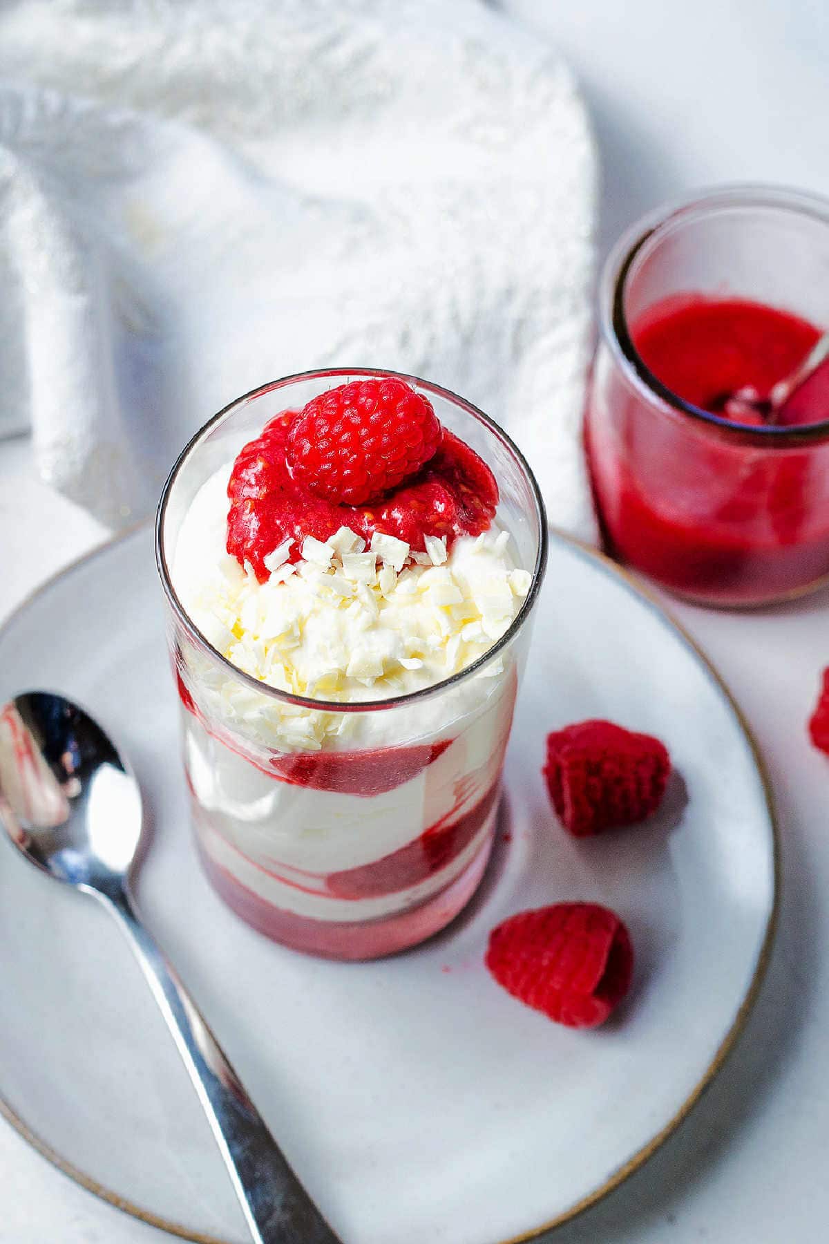 White Chocolate Mousse topped with raspberry dessert sauce and fresh raspberries on a table with a jar of raspberry coulis.