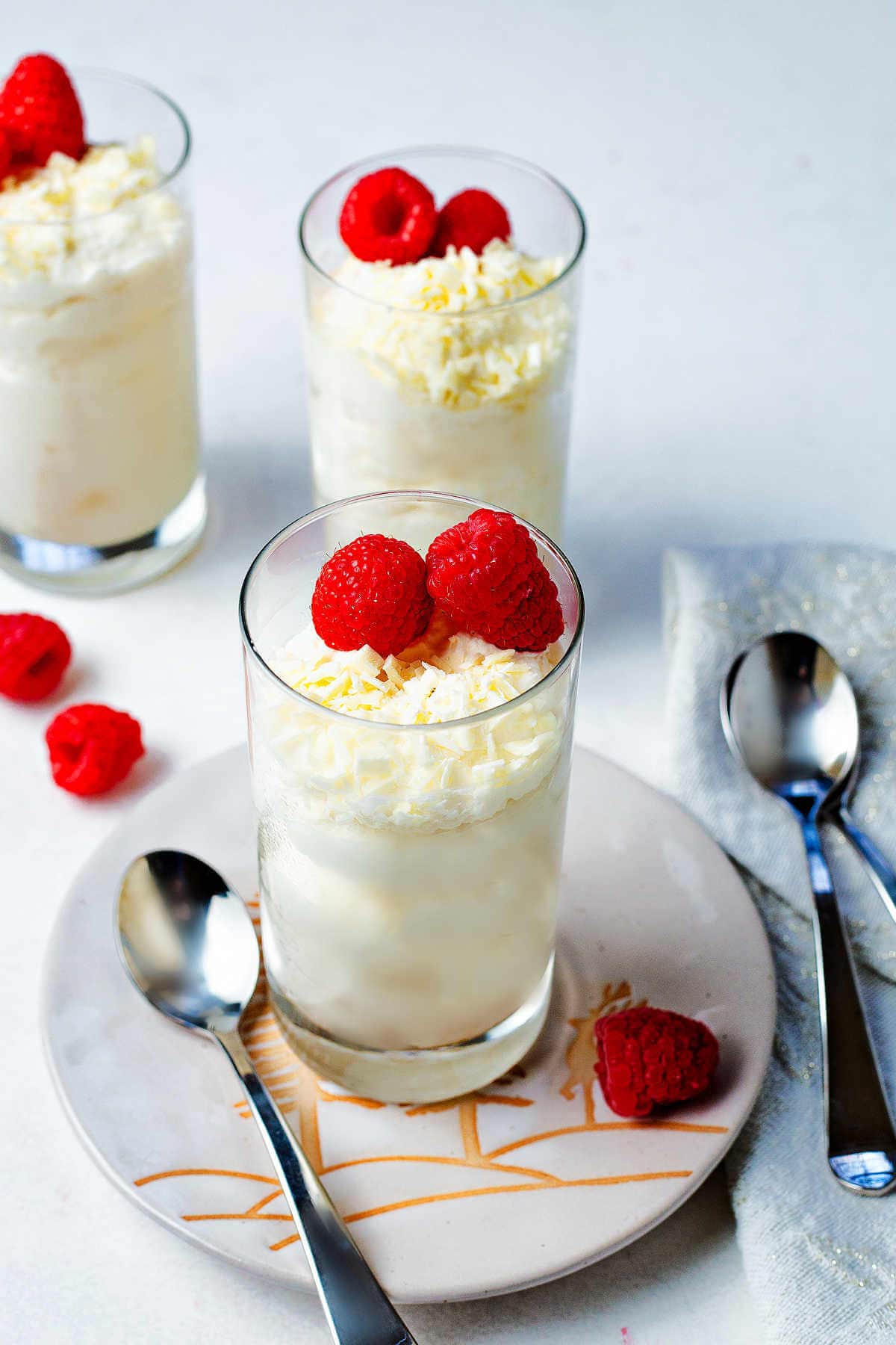 Three servings of whit chocolate mousse on a table with fresh raspberries.