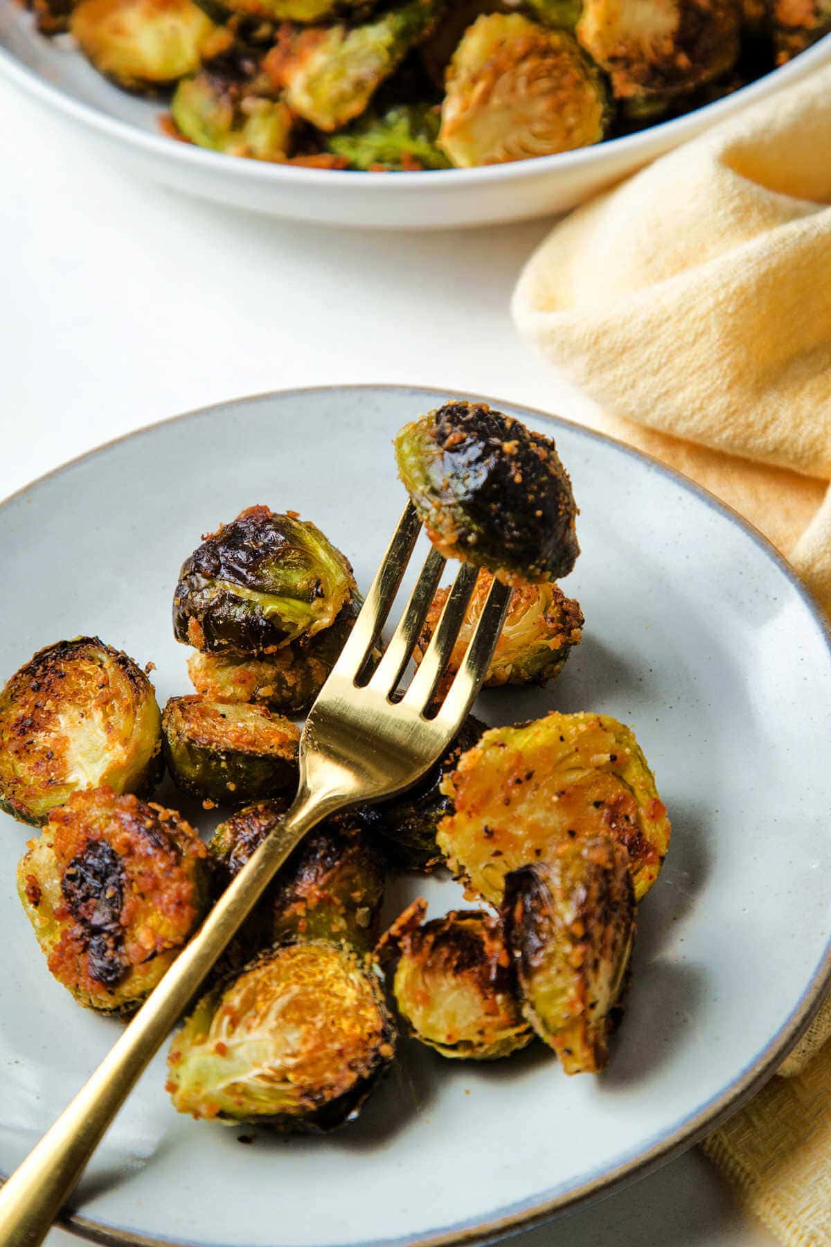 A fork spearing a Brussels sprout roasted with Parmesan cheese on a plate.