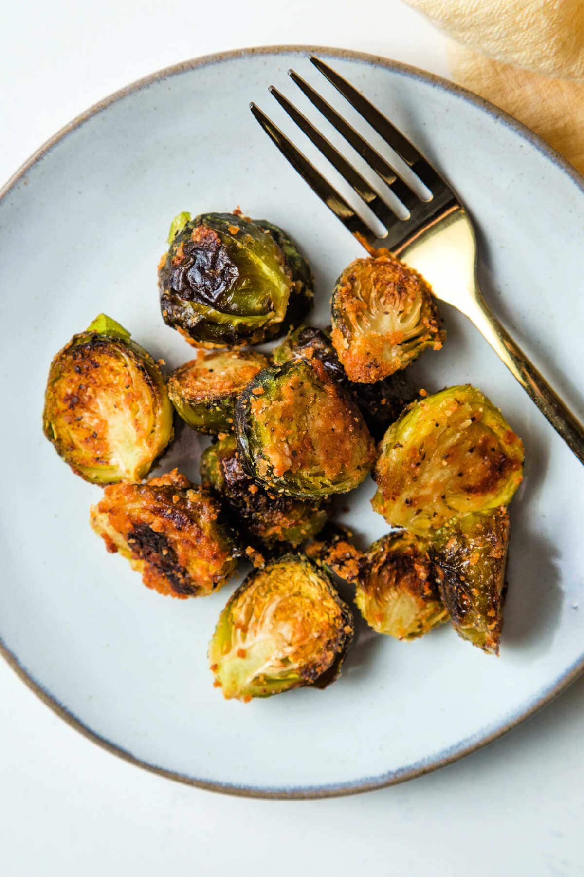 A serving of Brussels sprouts on a plate with a fork on a table.