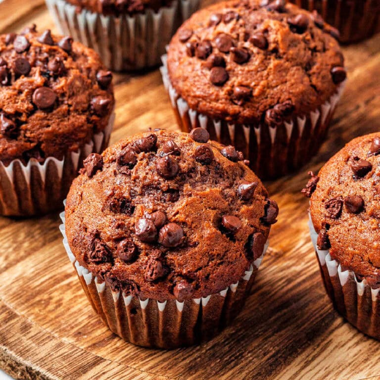 Chocolate banana muffins studded with chocolate chips on a wooden board.