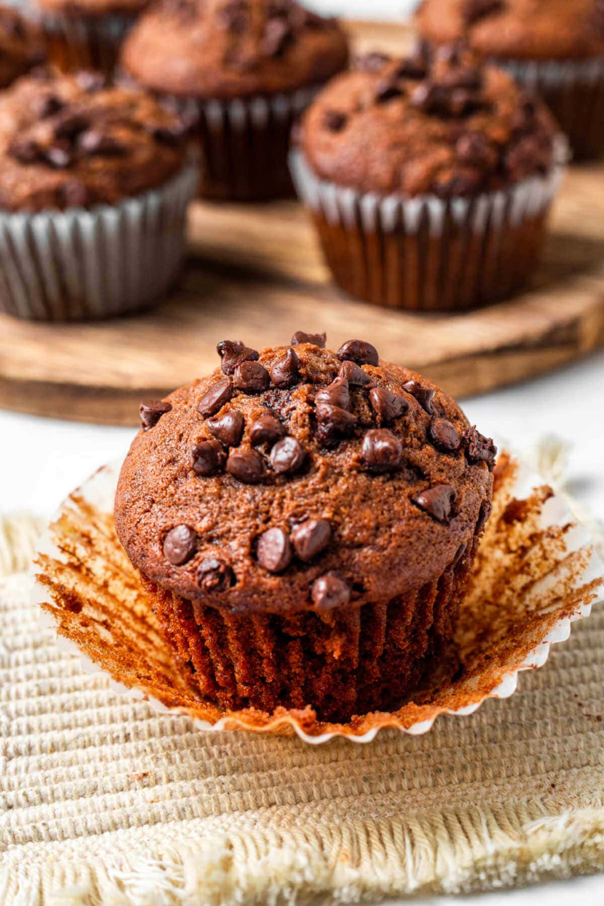 A double chocolate banana muffin sitting on a peeled away paper liner on a table.