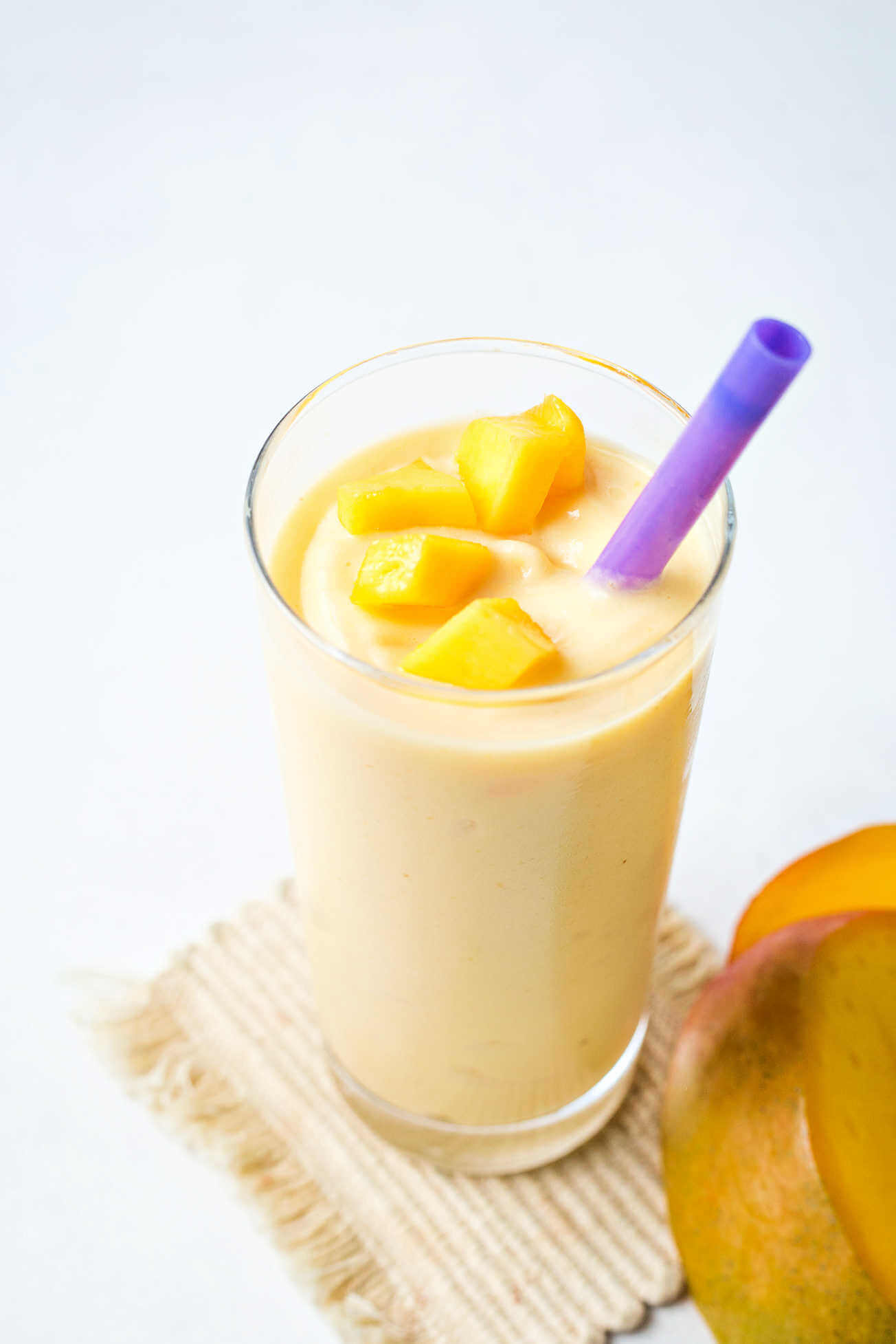 A mango smoothie topped with chopped mango pieces in a glass with a purple straw.