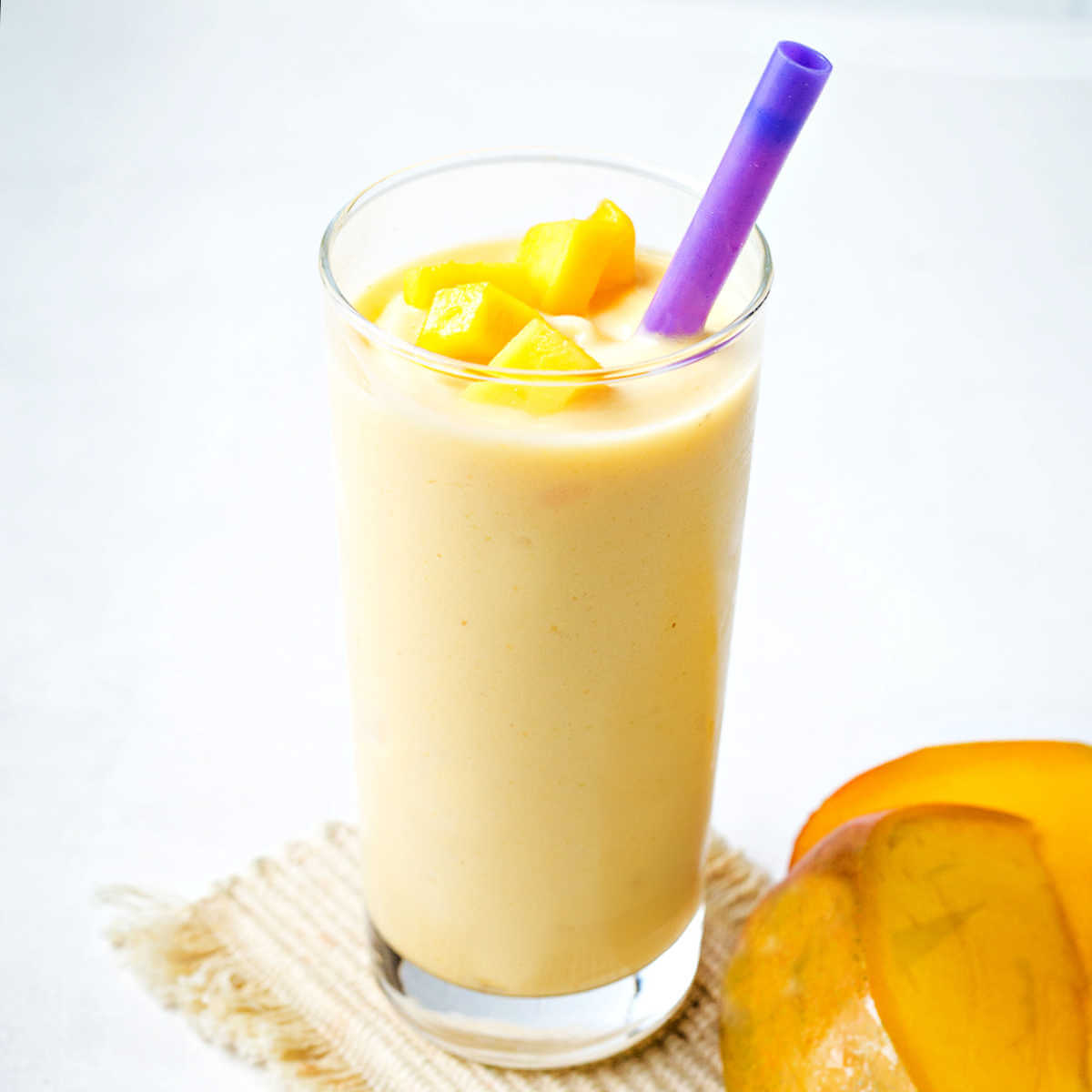 A mango smoothie topped with chopped mango pieces in a glass with a purple straw.