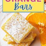 Orange bars stacked on top of each other on a plate with orange slices and powdered sugar dusted on top.