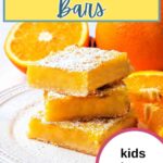 Orange bars stacked on top of each other on a plate with orange slices and powdered sugar dusted on top.