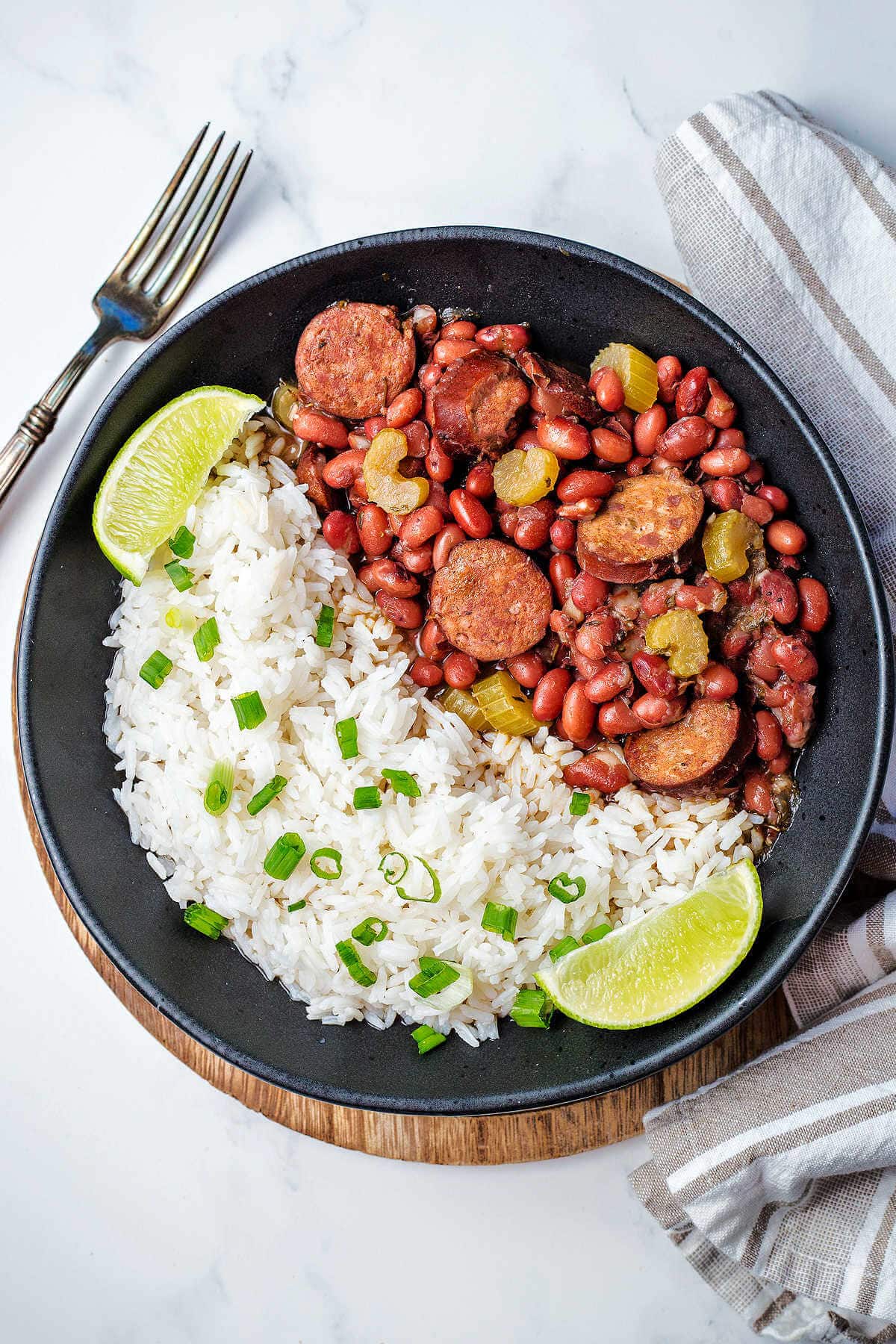 A bowl of red beans and rice on a table with a fork and napkin to the side.