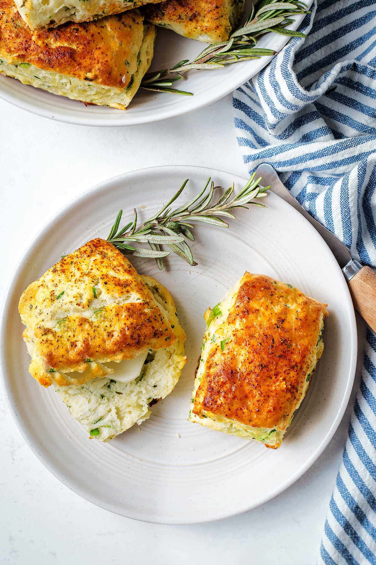 Two ricotta scones on a plate with a pat of butter and rosemary sprigs.