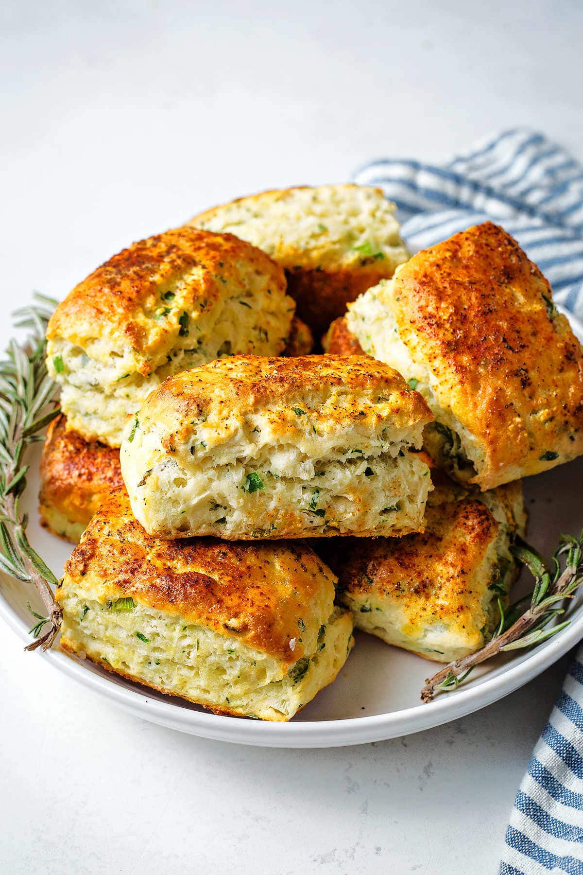 Savory scones piled on a plate with sprigs of rosemary on a table.